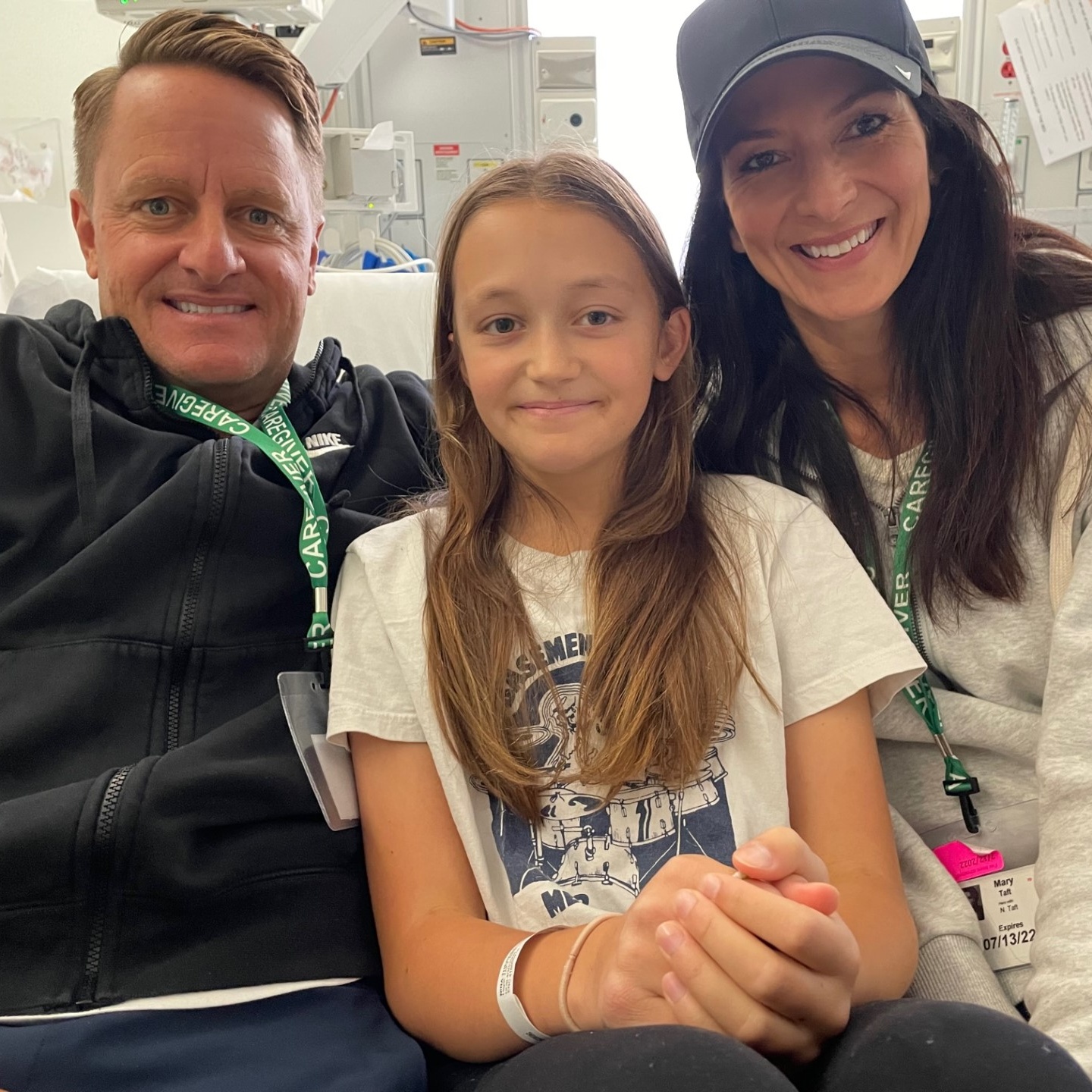 An adult man on the left, a young teen girl in the middle and an adult women on the right in a hospital bed.