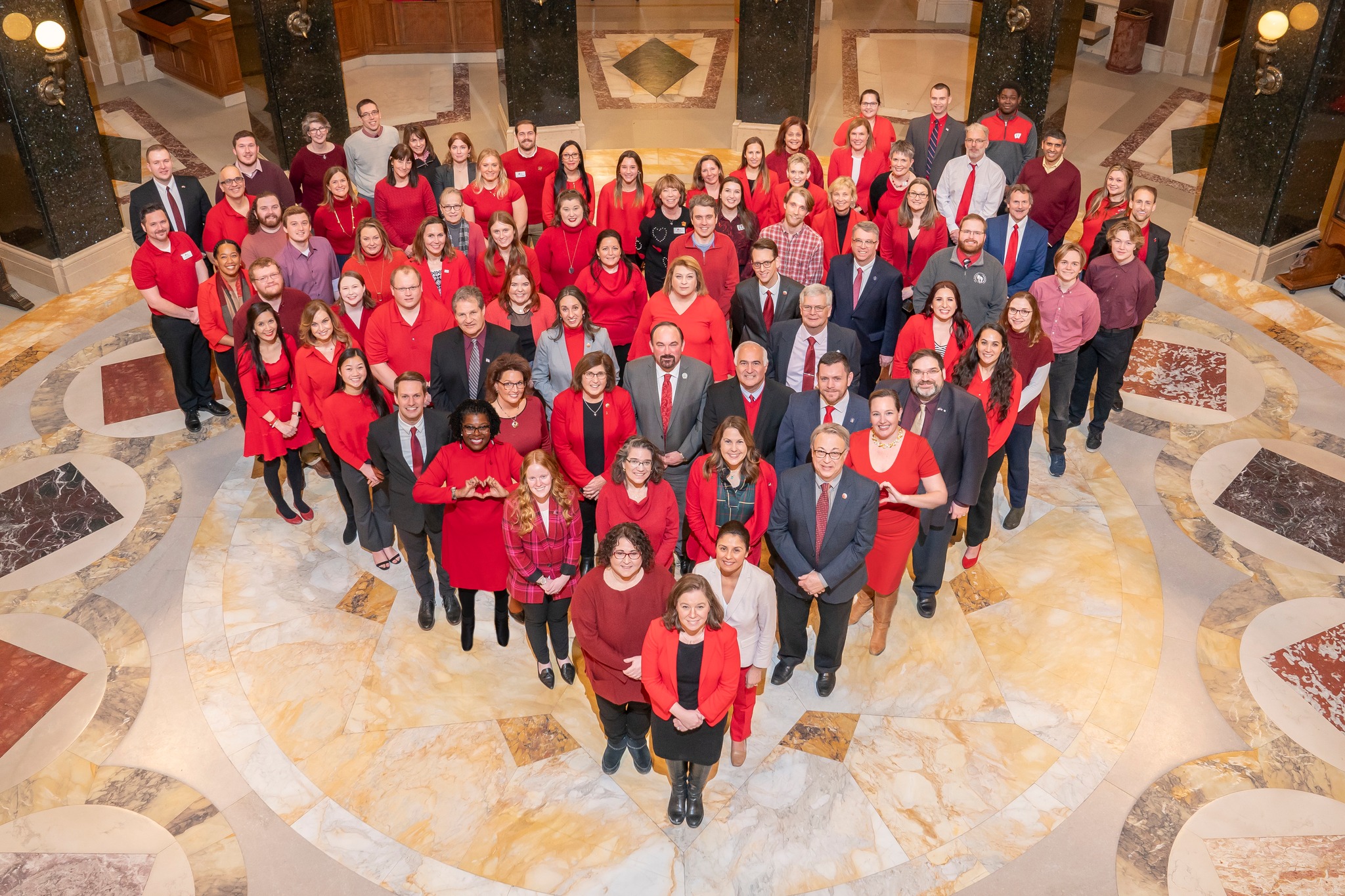 Advocates in the Wisconsin State Capitol standing in the shape of a heart, everyone is wearing red clothing.